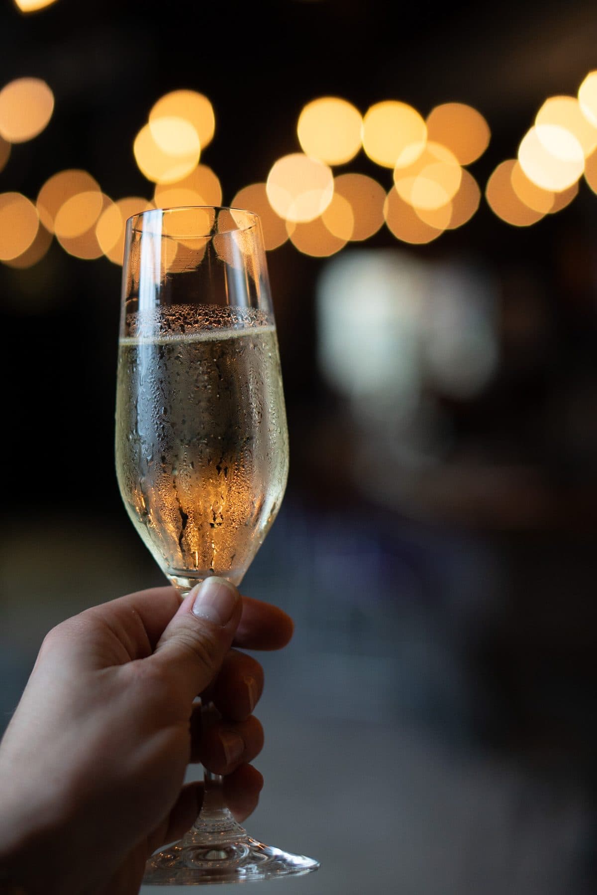 A glass of bubbly raised under the string lights at Vin Master