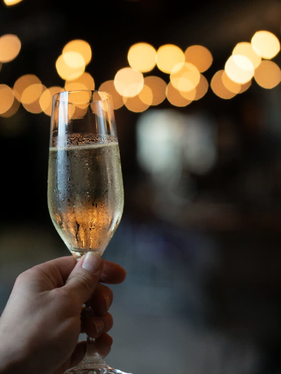 A hand raising a glass of sparkling wine at Vin Master under the string lights