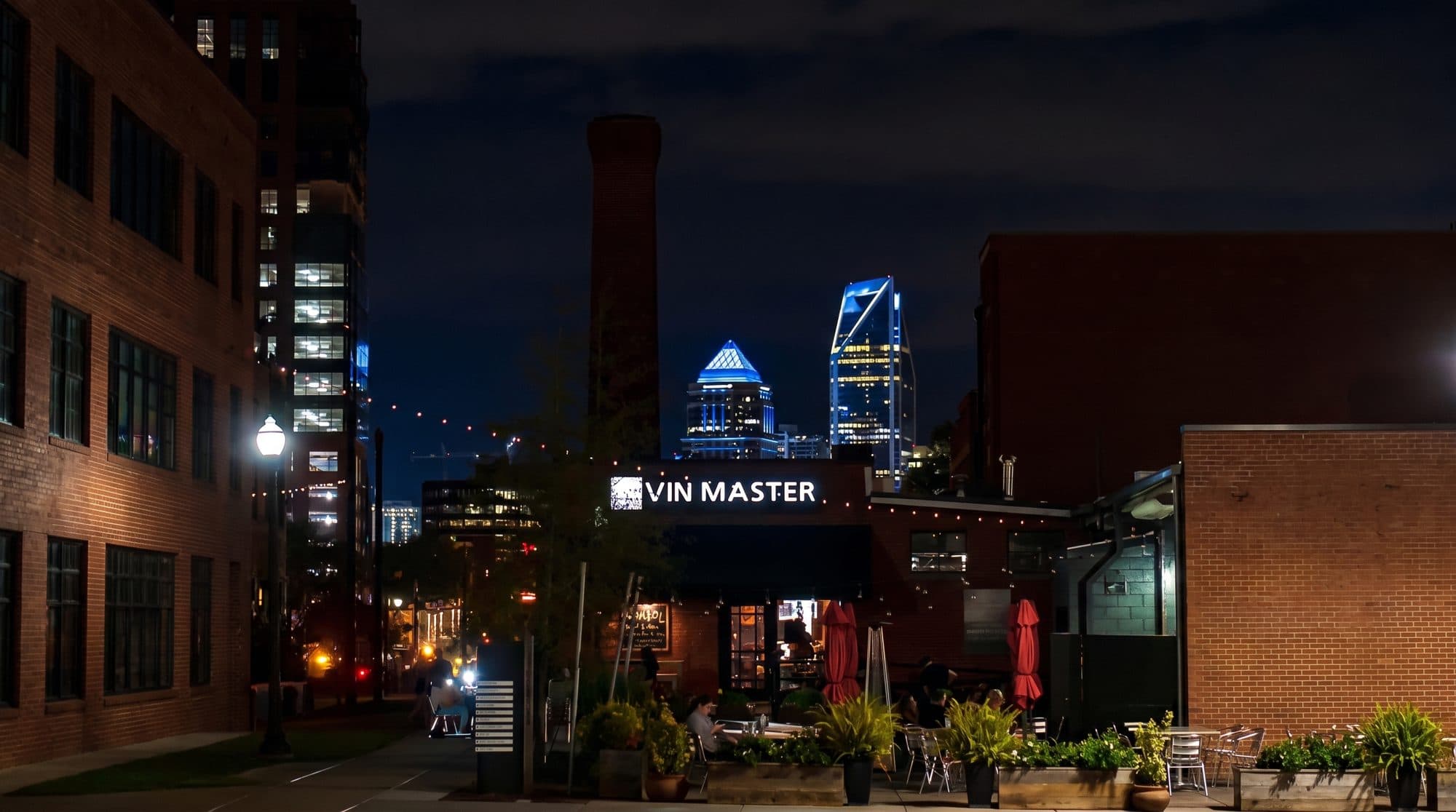 Vin Master storefront at night with the Charlotte skyline behind it