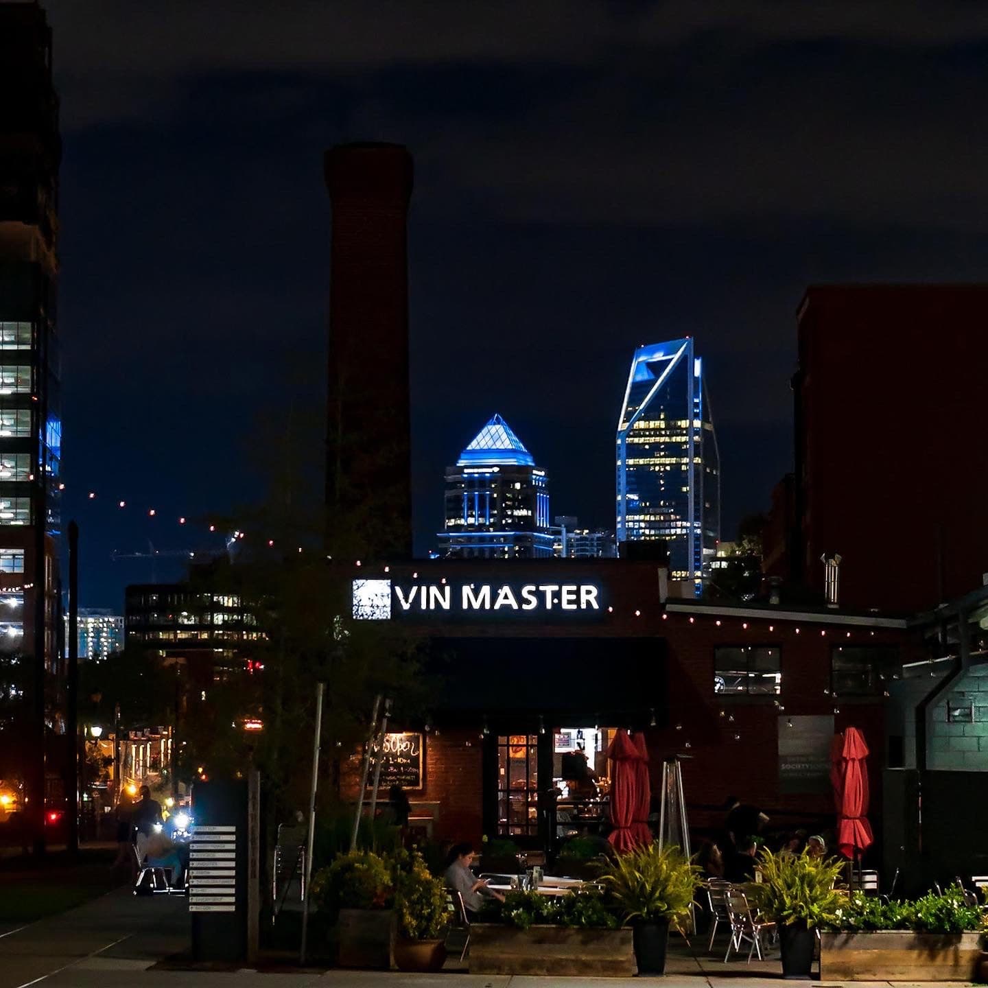 Vin Master storefront at night with the Charlotte skyline behind it